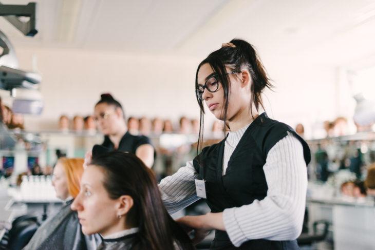Opiskelijat leikkaavat asiakkaiden hiuksia parturi-kampaamo Helmessä.