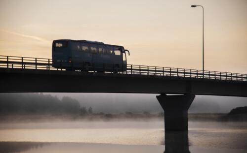Linja-auto ylittää sillan auringonnousussa.