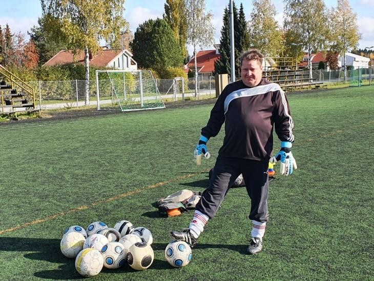 Maalivahdin varusteisiin pukeutunut lehtori Juha Heikkilä odottaa kentällä jalkapallojen kanssa.