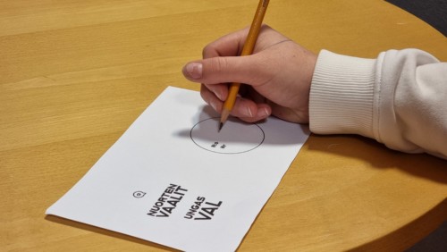 Opiskelijan käsi on valmiina kirjoittamaan numeron vaalilipukkeeseen.