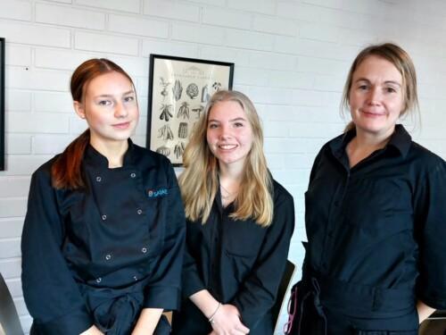 Opiskelijat Petra Haavisto ja Jenna Malonen työvaatteissa Tiina Aaltosen kanssa opetusravintola Ruukun ravintolasalissa.