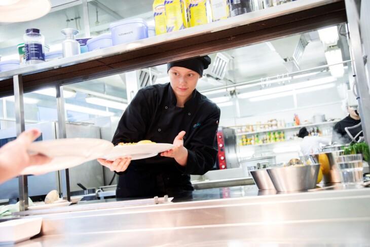 opiskelija antaa valmiin ruoka-annoksen keittiössä